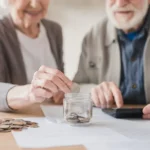 Pareja de adultos mayores ahorrando monedas en un frasco mientras revisan sus cuentas para la jubilación