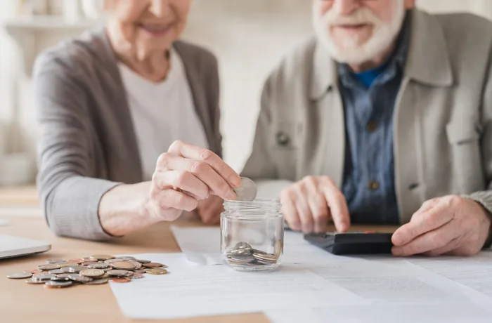 Pareja de adultos mayores ahorrando monedas en un frasco mientras revisan sus cuentas para la jubilación