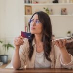 Mujer con tarjeta de crédito y celular evaluando una decisión financiera, mitos sobre el manejo del dinero