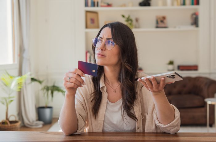 Mujer con tarjeta de crédito y celular evaluando una decisión financiera, mitos sobre el manejo del dinero