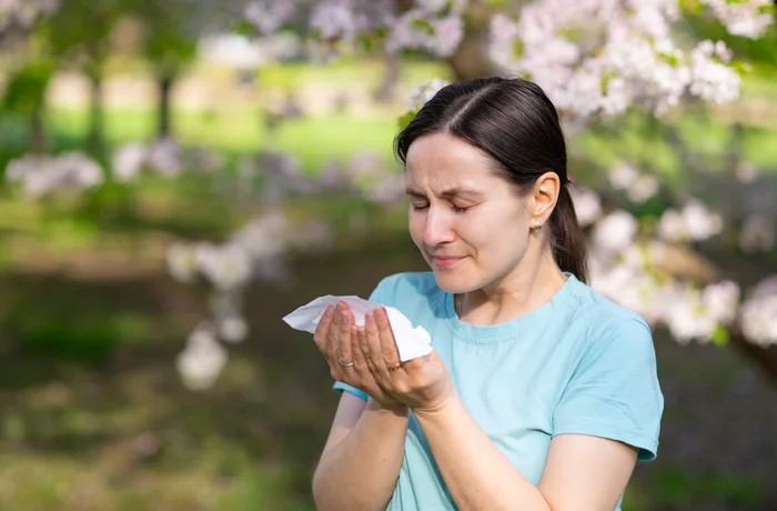 Mujer con alergia primaveral estornudando bajo árboles en flor